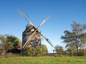 Traditional windmill in front of a blue sky, surrounded by trees and greenery, tower windmill, En,
