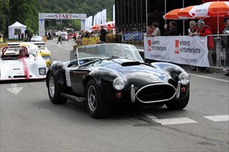 A black classic convertible racing car prepares for the start, spectators in the background,