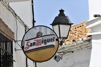 Solabrena, A round beer advertising sign for San Miguel on a wall next to a lantern, Andalusia,