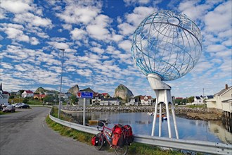 Packed touring bike in front of a huge globe and a harbour, Traena, Lovunden, Helgeland coast,