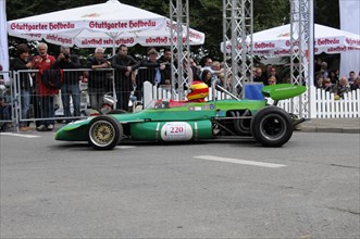 Green Formula racing car with number 220 on the race track in front of a crowd of spectators,