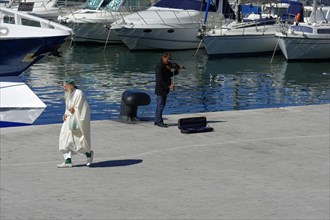 A street musician performs for an audience on a sunny harbour promenade, Marseille, Departement