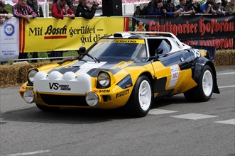 A yellow sports car with the number 184 drives past spectators during a race, SOLITUDE REVIVAL