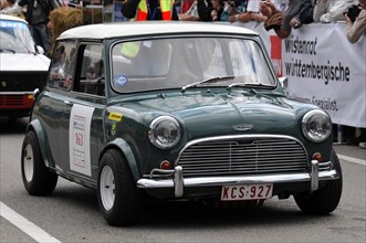 A green classic Mini with a racing number drives past spectators at a car race, SOLITUDE REVIVAL