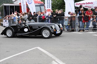 A black convertible classic car at a racing event with spectators in the background, SOLITUDE