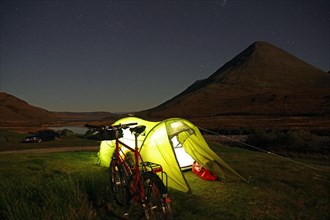 Tent illuminated with a torch in front of rugged mountains, bicycle, Cullins, Isle of Skye,
