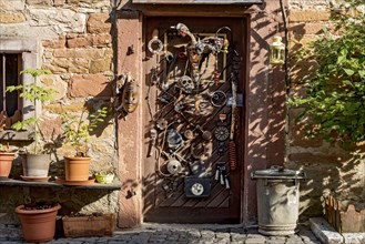 Old half-timbered house, whimsically decorated, flower pots, door with masks, skulls, engine parts,