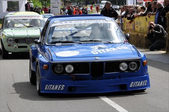 A blue BMW racing car with Gitanes branding at a road race, surrounded by spectators, SOLITUDE