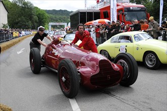 A red vintage racing car is pushed by a man in a race while spectators watch, SOLITUDE REVIVAL
