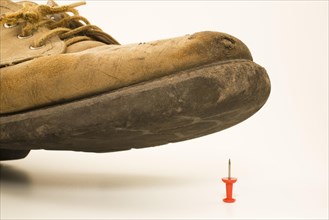 Close-up of elevated old and worn safety work shoe about to step on red upright pushpin with sharp