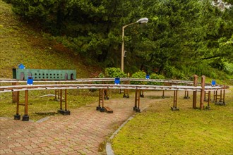 Miniature outdoor train station with benches and lampposts surrounded by trees on a cloudy day, in