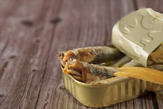 Tin can with tasty sprats with a wooden fork on a wooden table
