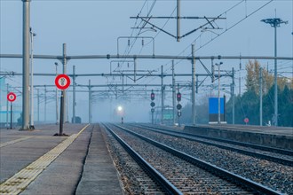 Empty train platform at a station on a foggy day with overhead electrical equipment and light of