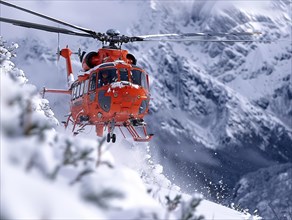 Ein roter Hubschrauber auf einer Rettungsmission in den Bergen bei winterlichen Bedingungen,