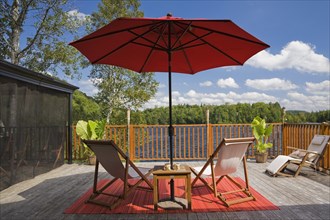 Black fishnet gazebo with red canvas cloth parasol and wooden folding canvas chairs on red mat on