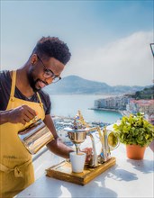 Happy person making coffee outdoors with a scenic coastal view in bright daylight, Vertical aspect