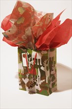 Close-up of Christmas gift bag with reindeer images and decorated with red silk paper on white