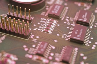 Close-up of pinkish lighted electronic computer circuit board, microchips, silver solder points and