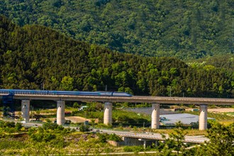 Train crossing a bridge in a mountainous area with trees on a bright sunny day, in South Korea