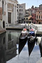 Two gondolas rest in the clear waters of a canal, surrounded by traditional Venetian architecture,