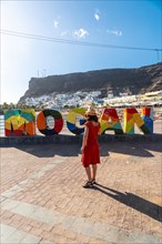 A woman in a red dress on the tourist sign in the coastal town of Mogan in the south of Gran