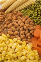 Close-up of mixed cooked vegetables that include brown baked beans, green peas, orange carrots and