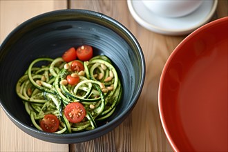 Green zucchini noodles with pesto, cherry tomatoes and pine nuts in a vibrant red bowl, AI