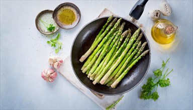 Simple still life with asparagus in a pan and simple ingredients on a light-coloured background,