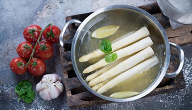 A pot of asparagus and lemon slices surrounded by fresh ingredients, fresh white asparagus in a