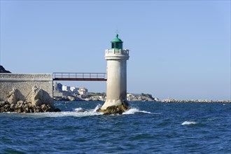 Lighthouse stands on rocky coast with rough sea and clear sky, Marseille, Departement