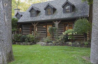 White chinked log cabin home facade with grey weathered cedar shingles roof, three dormer windows