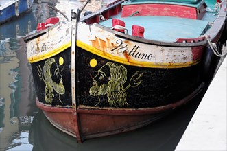 The painted front of a boat with a lion's head motif on calm water, Burano, Venice, Veneto, Italy,