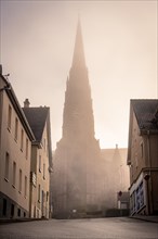 Morning fog envelops a church spire in an urban scene, faint sunlight penetrates, sunrise, Nagold,