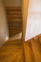 Narrow steep and twisting pine wood staircase with natural stained steps and rustic log wall