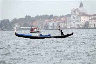 Gondolier paddling a gondola against the backdrop of historic buildings, Venice, Veneto, Italy,
