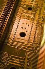 Close-up of golden orange and yellow lighted electronic computer circuit board with silver solder