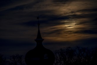 Full moon behind clouds above the steeple of the Protestant church in Braunschweig-Timmerlah,