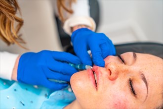Woman receiving an injection to increase volume in the lips in a facial beautification procedure at