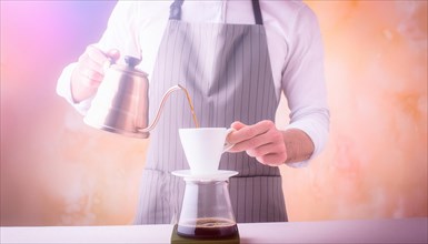 Elegant man in an apron carefully pouring hot water from a kettle into a coffee filter with steam