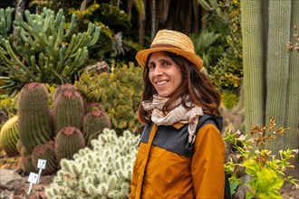 A smiling tourist woman enjoying in a tropical botanical garden with many captus