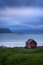 A red wooden hut on the sandy beach of Ramberg (Rambergstranda), sea and mountains. At night at the