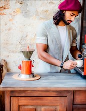 Fashionista man in a red hat prepares coffee with an espresso machine and a red coffee maker,