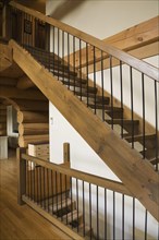 Brown stained wooden staircase with wrought iron railing leading to upstairs floor from living room