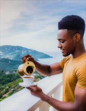 African young stylish Man pouring coffee from a golden coffee maker on a terrace with a serene