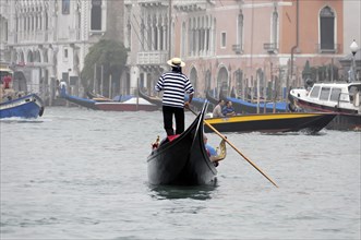 A gondolier steers a gondola through a canalised waterway in Venice, Venice, Veneto, Italy, Europe