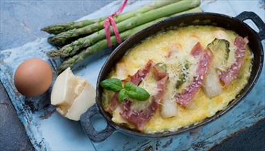 Hearty asparagus casserole with ham and egg served on a rustic wooden board, asparagus casserole