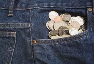 Close-up of US 5, 10, 25 cent coins bulging out of the front pocket of a pair of blue denim jeans,