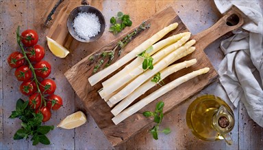 An arrangement of white asparagus on a board with ingredients for cooking on a rustic background,