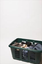 Close-up of green plastic laundry hamper or basket filled with various dirty clothes that includes
