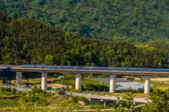 High-speed train on a bridge with green rolling hills under the bright sunlight, in South Korea